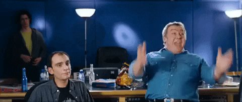 Movie gif. Gregor Fisher as Joe in Love Actually raises his hands excitedly over his head like he's cheering for someone.