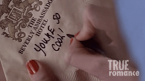 Movie gif. Scene from True Romance. A woman with red nail polish writes a note and a heart on a Beverly Ambassador Hotel napkin that reads, “You’re so cool!”