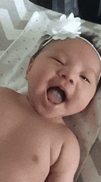 Video gif. A cute, dimpled baby with a bow on her head smiles at us and winks.