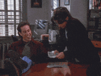 Seinfeld gif. Jerry sits with his feet on a table and a cigar in his mouth, smiling and nodding as Julia Louis-Dreyfus counts out cash in front of him, looking annoyed.