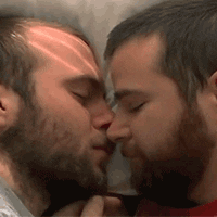 Video gif. We see a close up of two young men laying down together, nose to nose. One sweetly strokes the other's chin with his hand. Awwww.