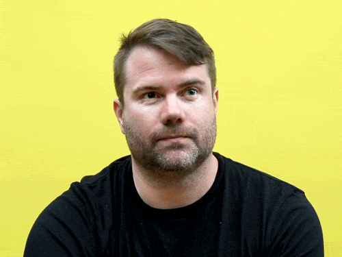 Video gif. Man wearing a black shirt ponders something, then nods is if to say, “If you say so.”