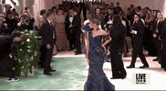Met Gala 2024 gif. Zendaya wearing a peacock-colored Maison Margiela gown by John Galliano embellished with true-to-life grapes and hummingbirds, struts down the carpet striking pose after pose, sticking the landing with brooding poise.