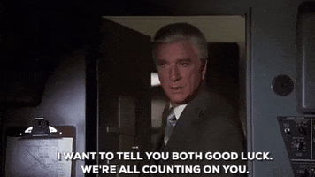 Movie gif. Leslie Nelson as Dr. Rumack in Airplane leans through the cockpit door and nods firmly as he says, “I want to tell you both good luck. We're all counting on you.”