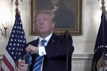 Political gif. Donald Trump appears against a formal Presidential background and in front of a microphone. Looking at us, he opens a bottle of water and lifts it to his lips as he tilts his head back, taking a small sip.