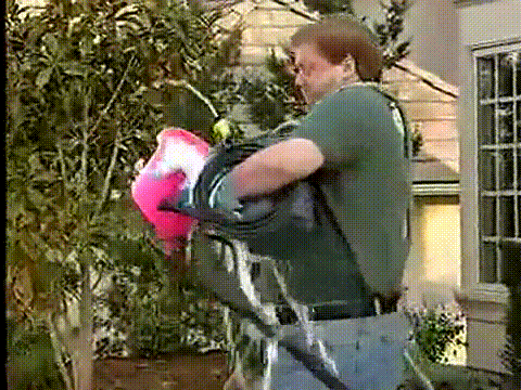 Video gif. Man struggles absurdly walking toward a car, carrying buckets of soapy water, a spraying hose, and other equipment, spilling everything and falling on the hood of the car.