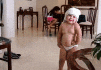 Video gif. A toddler wears underwear and a white shirt over their head. They claps and then shakes their chubby body. 