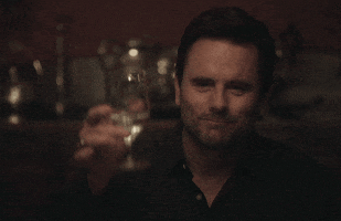 TV gif. Deacon Claybourne as Charles Esten sits at a dining table holding a glass of water in his hand. He looks down the table with a warm smile, and lifts his glass in celebration. He says, “Cheers.”