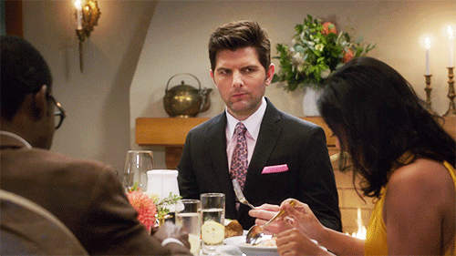 TV gif. Adam Scott as Trevor on the Good Place sits at a dining table with William Jackson Harper as Chidi across from him and Tiya Sircar as Vicky sitting next to him. While everyone eats, Trevor looks over at Vicky, chewing his food, and then suddenly the food falls out of his mouth.