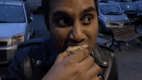 Celebrity gif. Aziz Ansari takes a bite of a pastry and scrunches his eyes in pleasure. We can nearly hear his moan as he chews and swallows, and it looks like the most delicious thing ever.