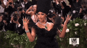 Met Gala 2024 gif. Slow motion closeup of the top of Cardi B's black strapless Windowsin gown decorated with a black wing motif. She brings her long pointy emerald green nails to hug around her waist as she looks to the side to pose for camera. She's wearing a diamond necklace with a giant teardrop emerald that drops to the top of her cleavage.