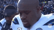 Sports gif. Standing on the field during a game, Brandon Mebane of the Los Angeles Chargers blows a kiss to the sky and exhales, his breath showing in the frigid air.