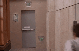 Video gif. A man runs quickly towards a door and then kicks him open. He stumbles backwards into the door and then runs down the hall. A woman watches him as he runs away. 