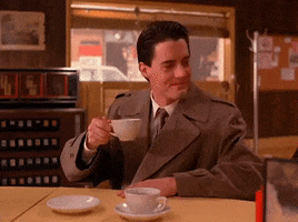 TV gif. Kyle MacLachlan as Agent Dale Cooper in Twin Peaks slides a cup of coffee down the diner counter.