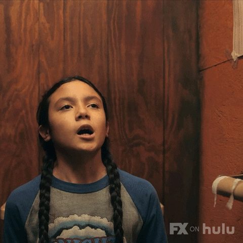 TV gif. A scene from Reservation Dogs. A boy sits on the toilet with an empty toilet paper roll on the wall. He calls out, “Hello I need help!”