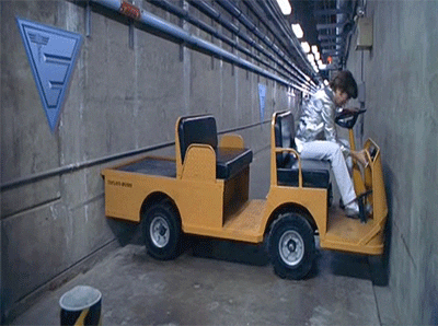 Movie gif. In a scene from "Austin Powers," Mike Myers as Austin Powers tries to complete a three-point turn in a tiny hallway while driving a large yellow cart. Despite his best efforts, he's not going anywhere.