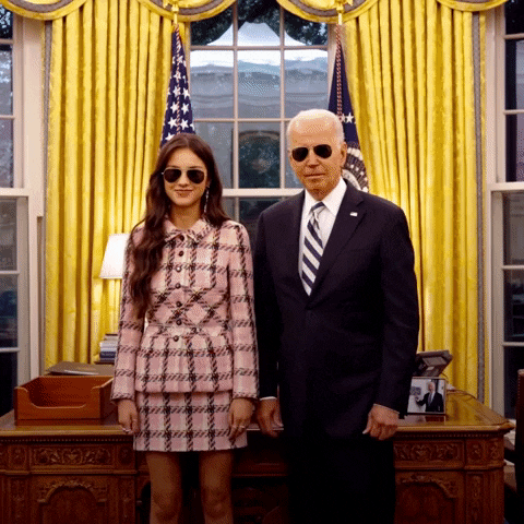 Political gif. Joe Biden and Olivia Rodrigo are standing in the Oval Office wearing aviators and they both give us a simultaneous double thumbs up.