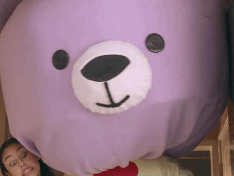 Video gif. A woman makes an apologetic face as she holds a massive purple teddy bear. Large text appears, "Sorry!"