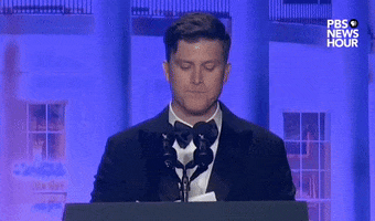 Video gif. Saturday Night Live's Colin Jost stands at a podium at the 2024 White House Correspondents' Dinner and takes a beat before acknowledging "Ok, I got one woo" while surveying the crowd.