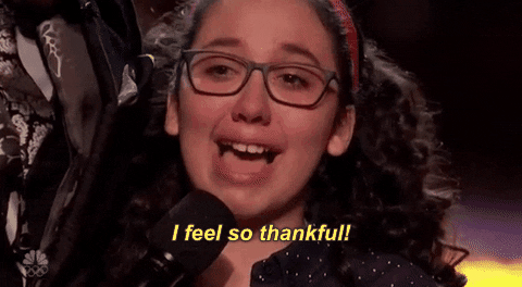 TV gif. Closeup on a young AGT contestant with curly hair and glasses, who looks like she's about to cry as she speaks into a microphone: Text, "I feel so thankful!"