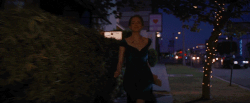 Movie gif. Emma Stone as Mia from La La Land runs down a sidewalk at night with a giddy smile, holding out her dark green dress by the skirt.