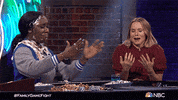 Reality TV gif. Kristen Bell on Family Game Fight cringes and covers her face to laugh as a woman next to her laughs with pie cream covering her head and chest.
