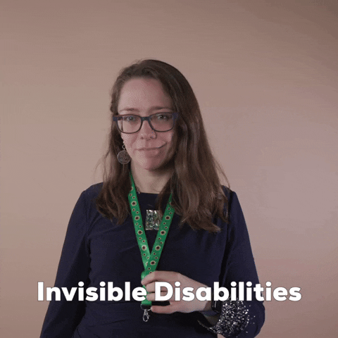 Reaction gif. A Disabled Latina woman with brown wavy hair and glasses shows off her green lanyard, presenting it with an ok sign and a knowing smile. Text, "Invisible disabilities."