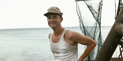 Movie gif. Tom Hanks as Forrest Gump laughs happily on the deck of a Bubba Shrimp boat before he sees something he's afraid of and ducks back behind cover. 