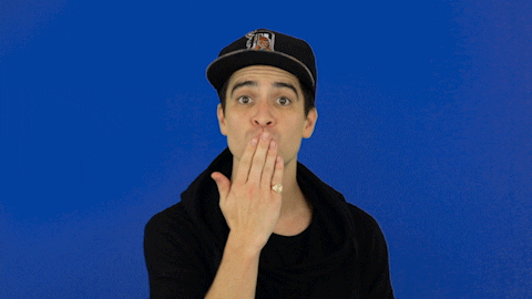 Celebrity gif. Brandon Urie from Panic! At the Disco blows a kiss then smiles against a blue background.