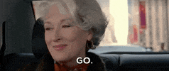 Movie gif. Meryl Streep as Miranda in The Devil Wears Prada. She sits in a car with a pleased smile on her face but when she realizes the car isn't moving, she gets annoyed. She coldly tells the driver, "Go," and rolls her eyes before putting sunglasses on.