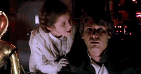 Star Wars gif. Carrie Foster as Princess Leia kisses Harrison Ford as Han Solo on the cheek and then sits down beside him, as he appears focused ahead.