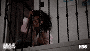 TV gif. Gabrielle Dennis from A Black Lady Sketch Show is sitting on the top floor of a home and clutching the bottom of the stair railing while yelling in fear, "Get out while you still can!"