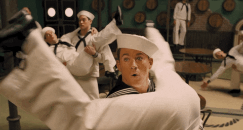 Movie gif. Channing Tatum as Burt Gurney in "Hail, Caesar!" dances in a sailor costume with a group of men. He holds one man upside down, the man's legs splayed wide and his, erm, buttocks in Tatum's face. Tatum looks up from the buttocks with an expression of surprise.