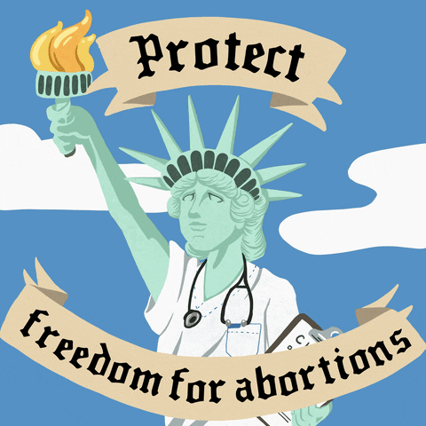 Digital art gif. Illustration of the Statue of Liberty wearing a nurse's scrubs and a stethoscope stands amid a blue sky and passing clouds. Tan ribbons above and below the statue contain text that reads, "Protect freedom for abortions."