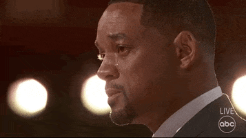 Celebrity gif. Will Smith at The Academy awards stands on stage. His eyes are red with tears and he wipes his nose, trying not to cry any harder. 