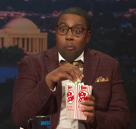 SNL gif. Kenan Thompson in thick rimmed glasses and a bow tie nods energetically while eating popcorn like he's excited or maybe a little anxious and intense.