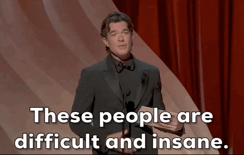 Oscars 2024 gif. With a deadpan expression, John Mulaney says, "These people are difficult and insane" while presenting at the Oscars.