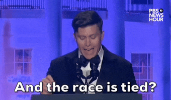 Video gif. Saturday Night Live's Colin Jost stands at a podium at the 2024 White House Correspondents' Dinner as incredulously yells "And the race is tied?"