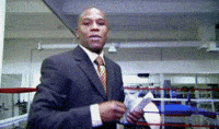 Sports gif. Floyd Mayweather is wearing a suit and is standing in a ring while tossing money at us. He looks very cocky and he throws one bill at at time.