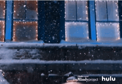 TV gif. We follow the falling snow to find Mindy Kaling as Mindy and Chris Messina as Danny in The Mindy Project kissing in the street amongst twinkly lights.