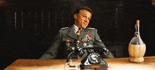 Movie gif. Christopher Waltz as Hans Landa in Inglorious Basterds leans back in his chair and holds his arms out to shrug. A rotary phone sits on the table in front of him.