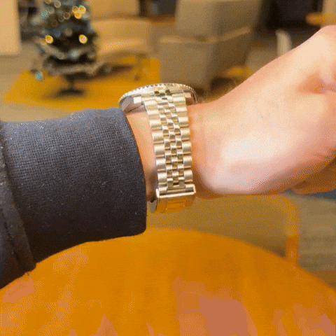 A person wearing a silver wristwatch indoors, with blurred background.