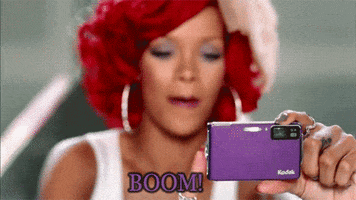 Celebrity gif. Rihanna holds a purple Kodak camera in her hand and taps the camera's screen, saying “boom!” as she takes the picture. 