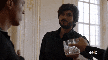 TV gif. A man cheers his companions, tapping one tumbler, then the other, exploring their eyes with stoic ambivalence. 