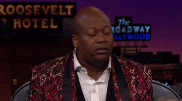 TV gif. Tituss Burgess as host of the Late Late Show holds his hands up in surrender and leans back in a guest chair as he shakes his head with a look of shock on his face.