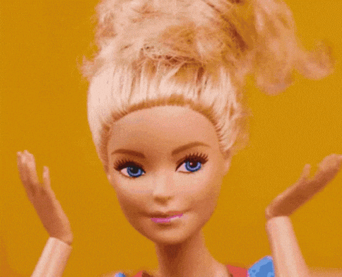 Video gif. A closeup on a Barbie doll with its hair up as its hands move to its mouth in "surprise".