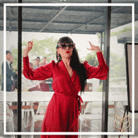 Video gif. A woman in a stylish red dress and large sunglasses dances elegantly as she lowers her sunglasses. Pink script reads, "Happy Birthday." 