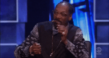 Celebrity gif. Snoop Dogg has a blunt in his mouth and he blows a bunch of smoke as he laughs.