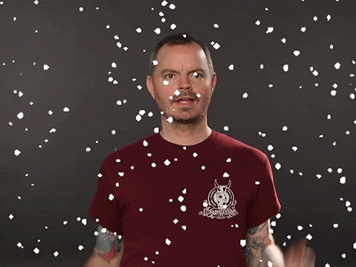 Video gif. A man looks around gleefully before smiling at us as digital snow falls around him. 