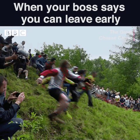 Reality TV gif. From the Great Cheese Chase, a group of people tumble over each other down a grassy hill, following a large wheel of cheese bouncing down the hill, as a line of onlookers watch from the side. Text, "When your boss says you can leave early."